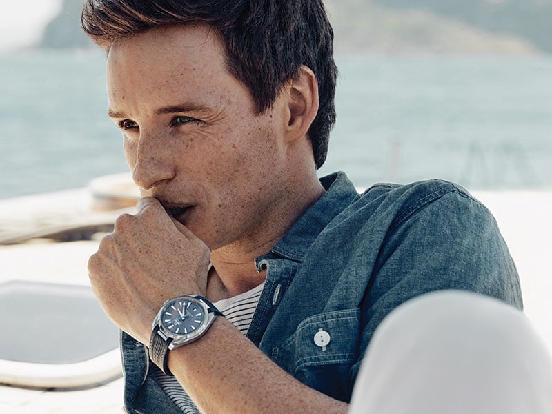 Eddie Redmayne, in a relaxed pose and wearing a Seamaster Aqua Terra, scans the horizon. 